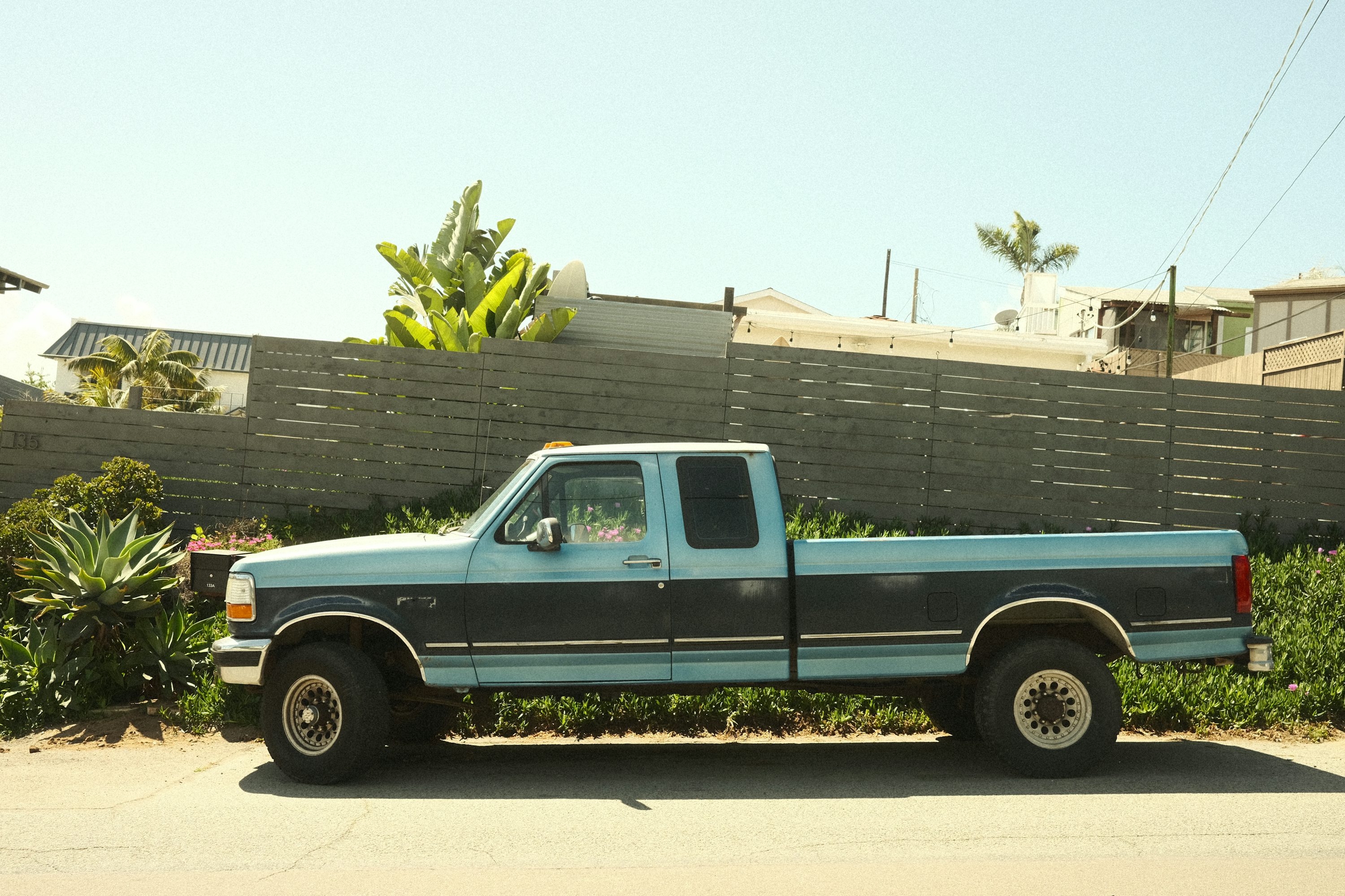 A blue pickup truck sits on a sunny street.