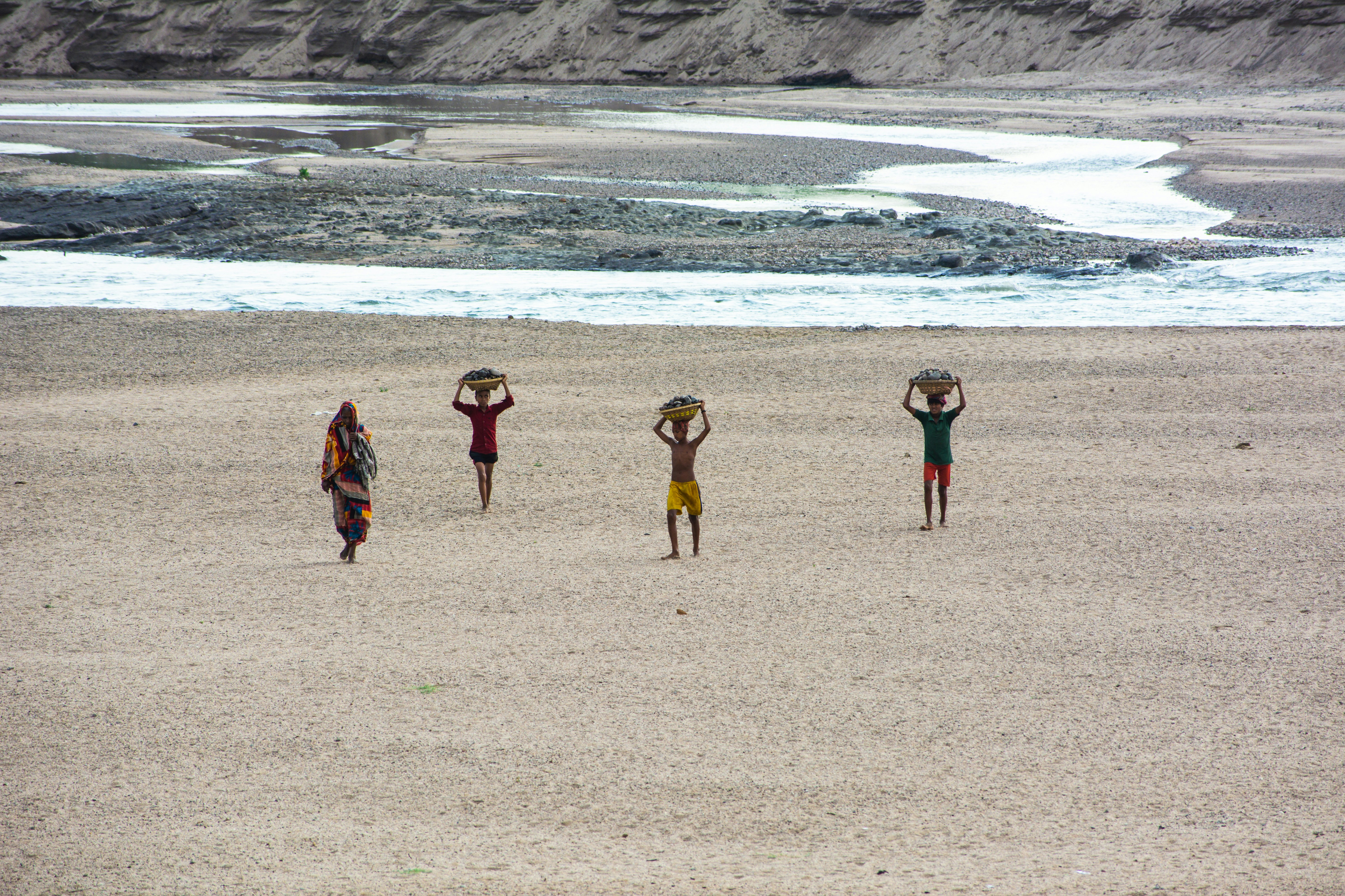 People carry baskets on their heads in a barren landscape.