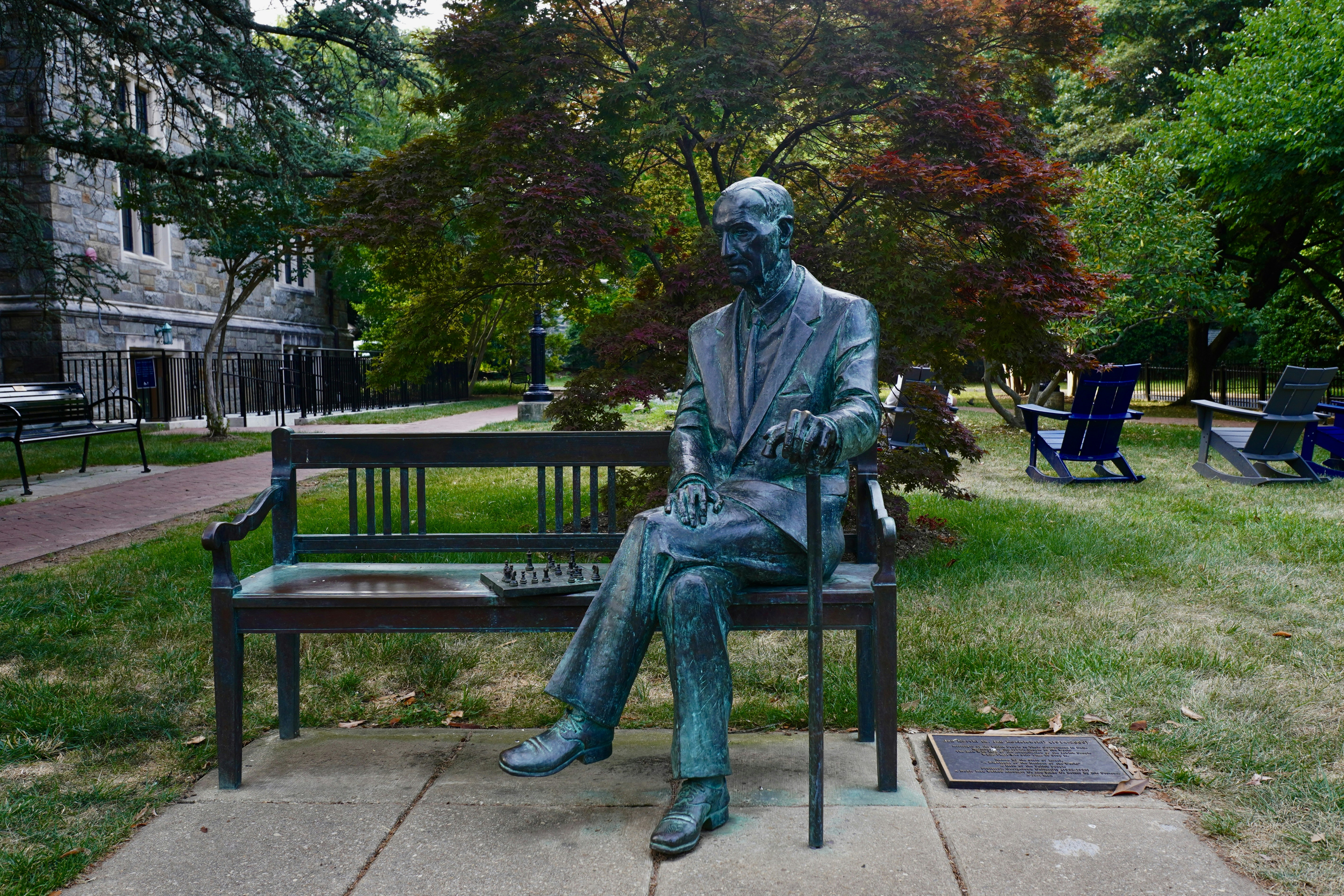 A statue sits on a bench outdoors.