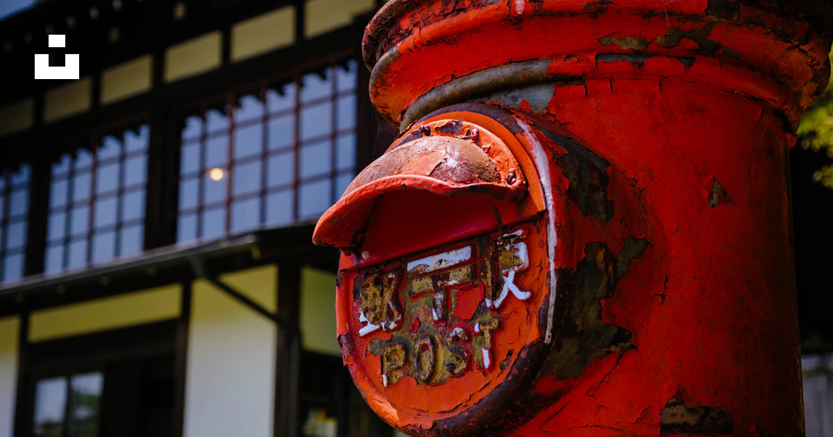 Red japanese postbox with traditional house in the background. photo ...