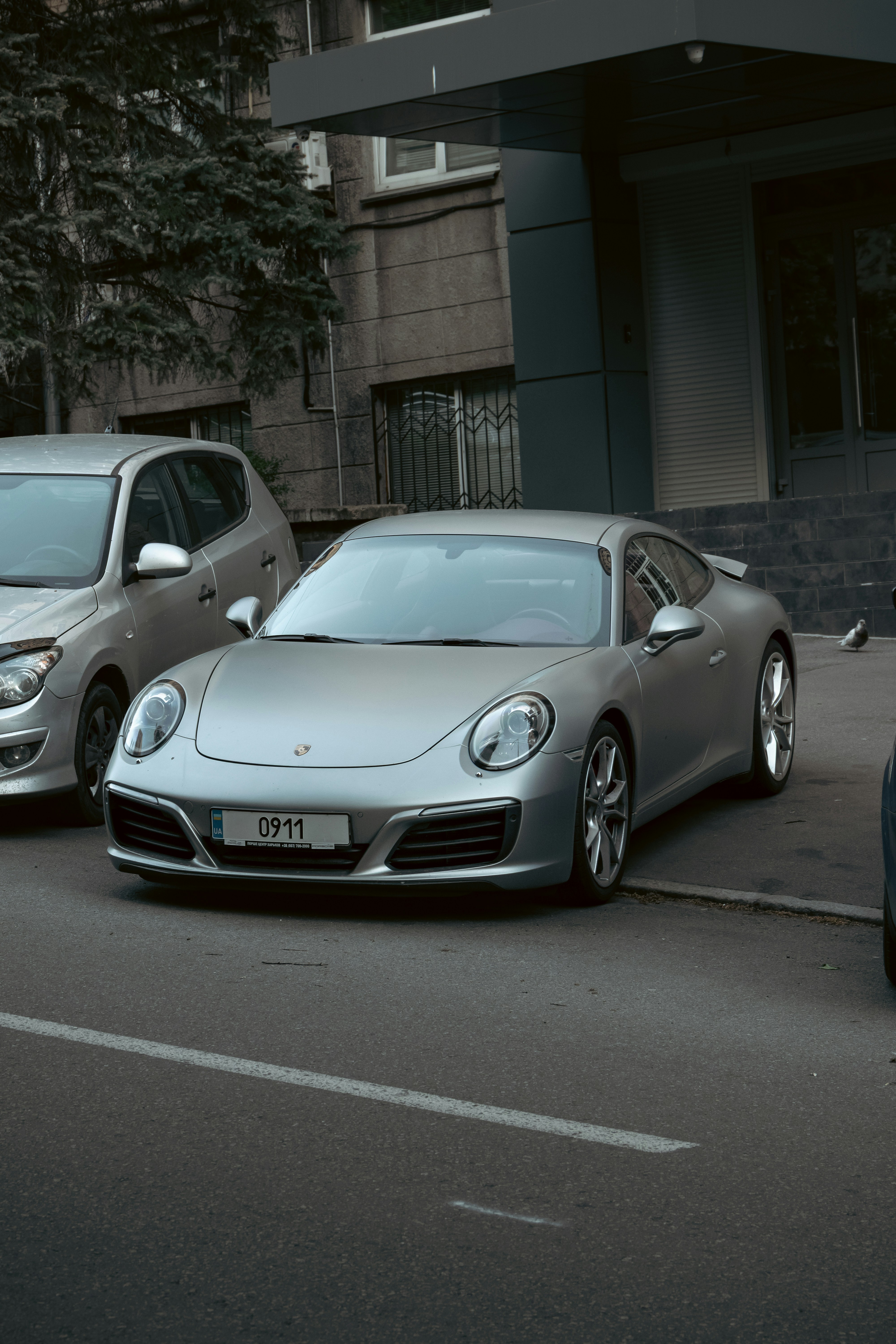 Um porsche prateado estacionado em frente a um prédio.