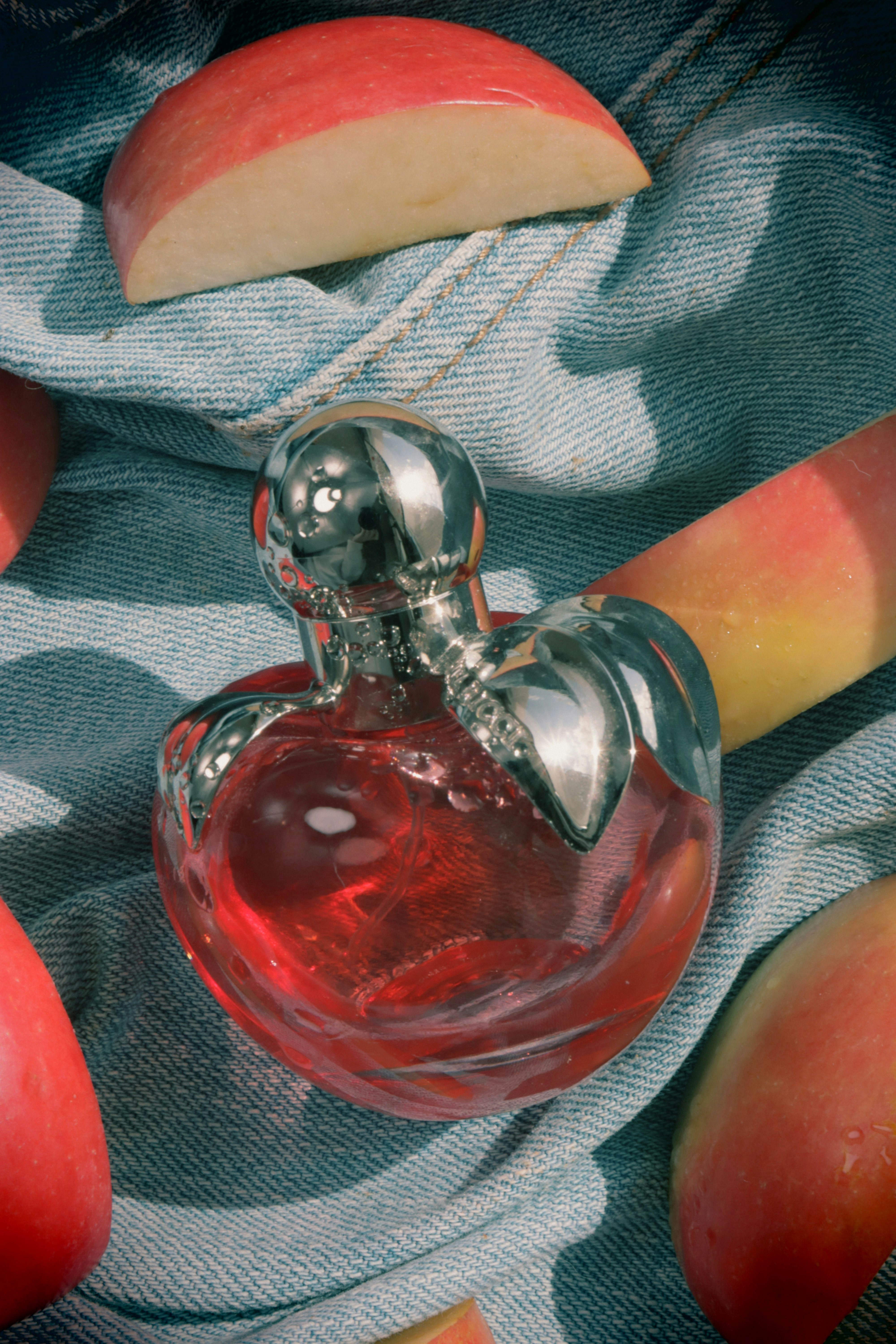 Perfume bottle and apple slices on denim fabric.