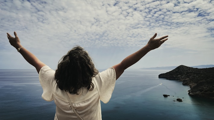 Woman with arms outstretched overlooking the ocean.