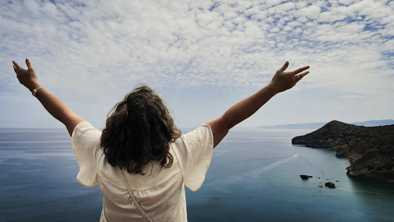 Woman with arms outstretched overlooking the ocean.