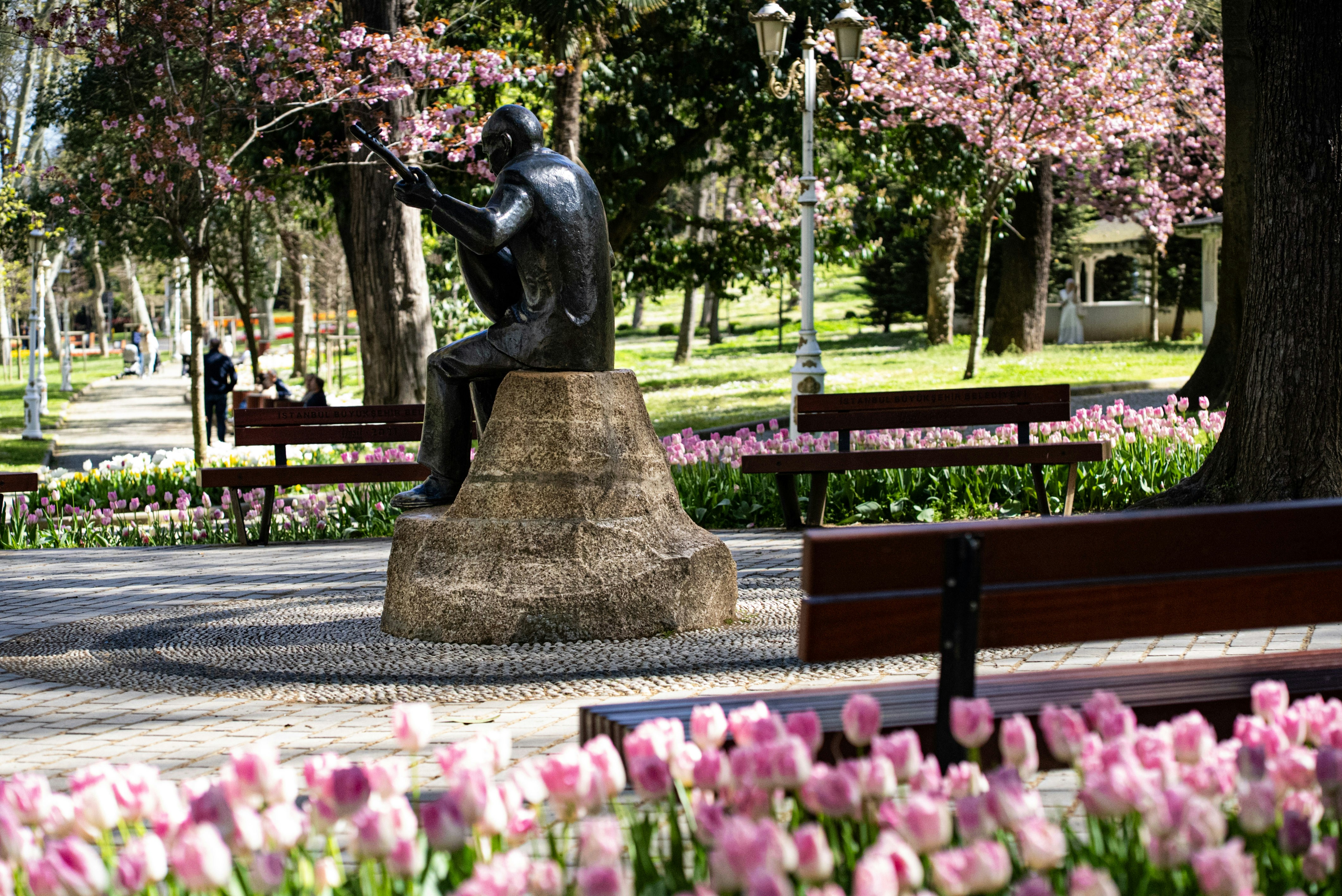 Statue sits in a park surrounded by spring blooms.