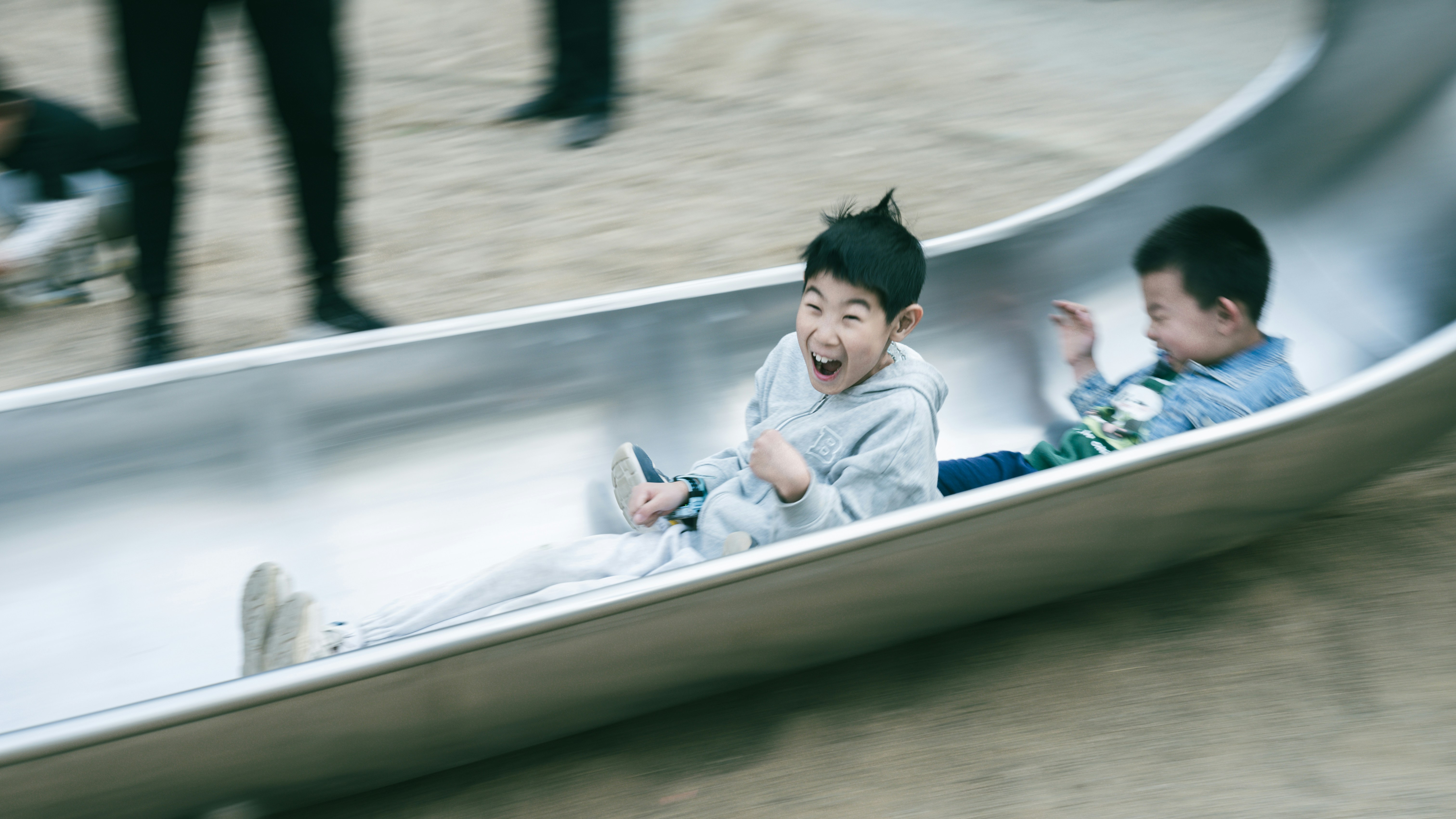 Two kids are joyfully sliding down a playground slide.
