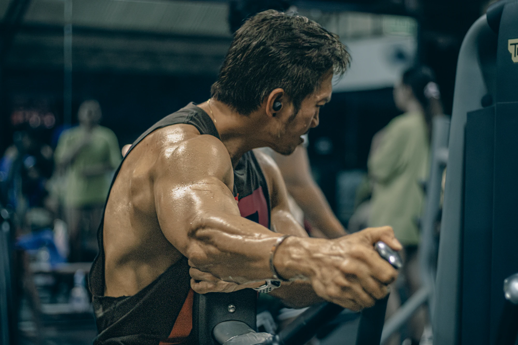 Mature man, sweat-soaked, mid-pull on cable — peak training effort