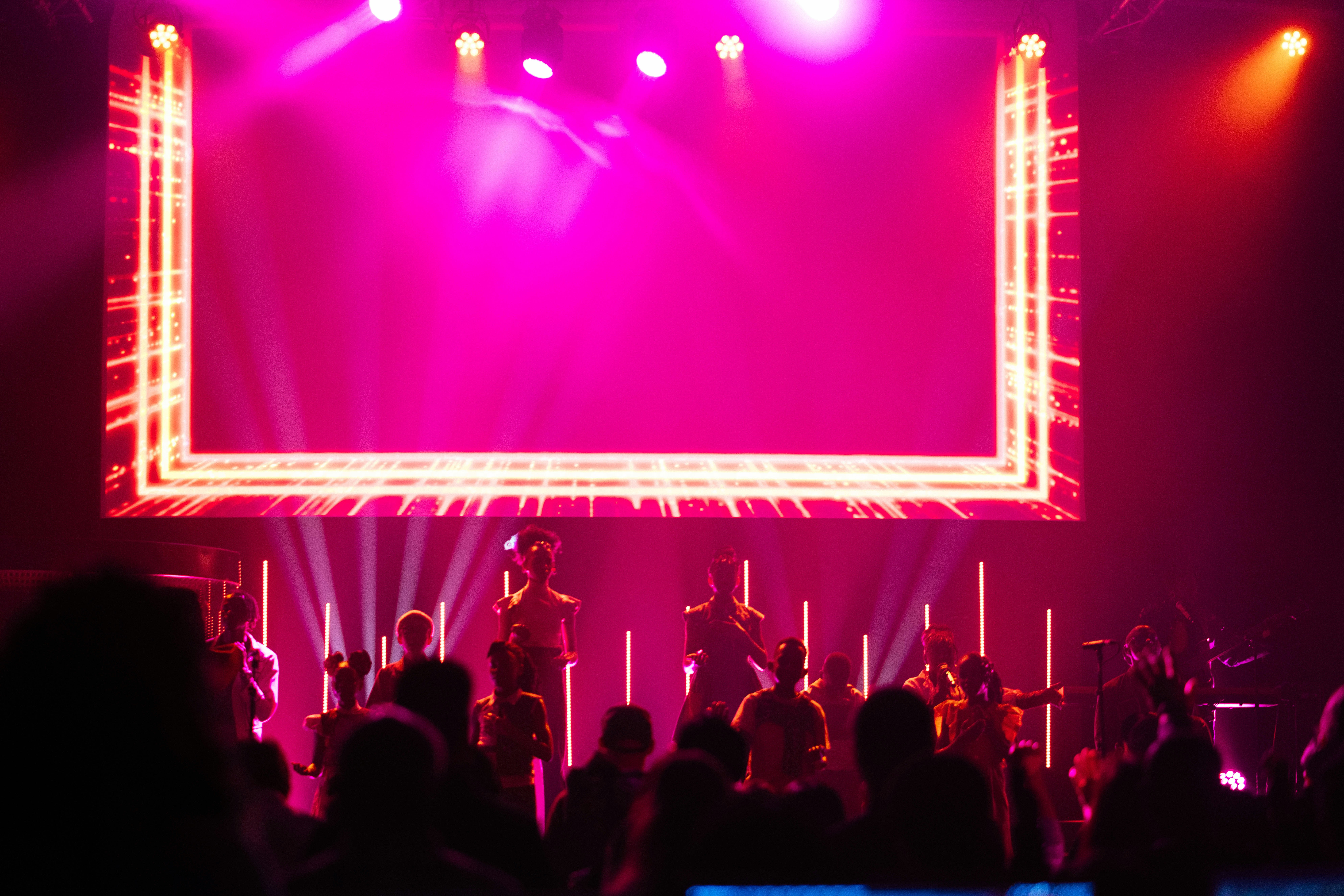 Uma banda se apresenta no palco com iluminação rosa brilhante.