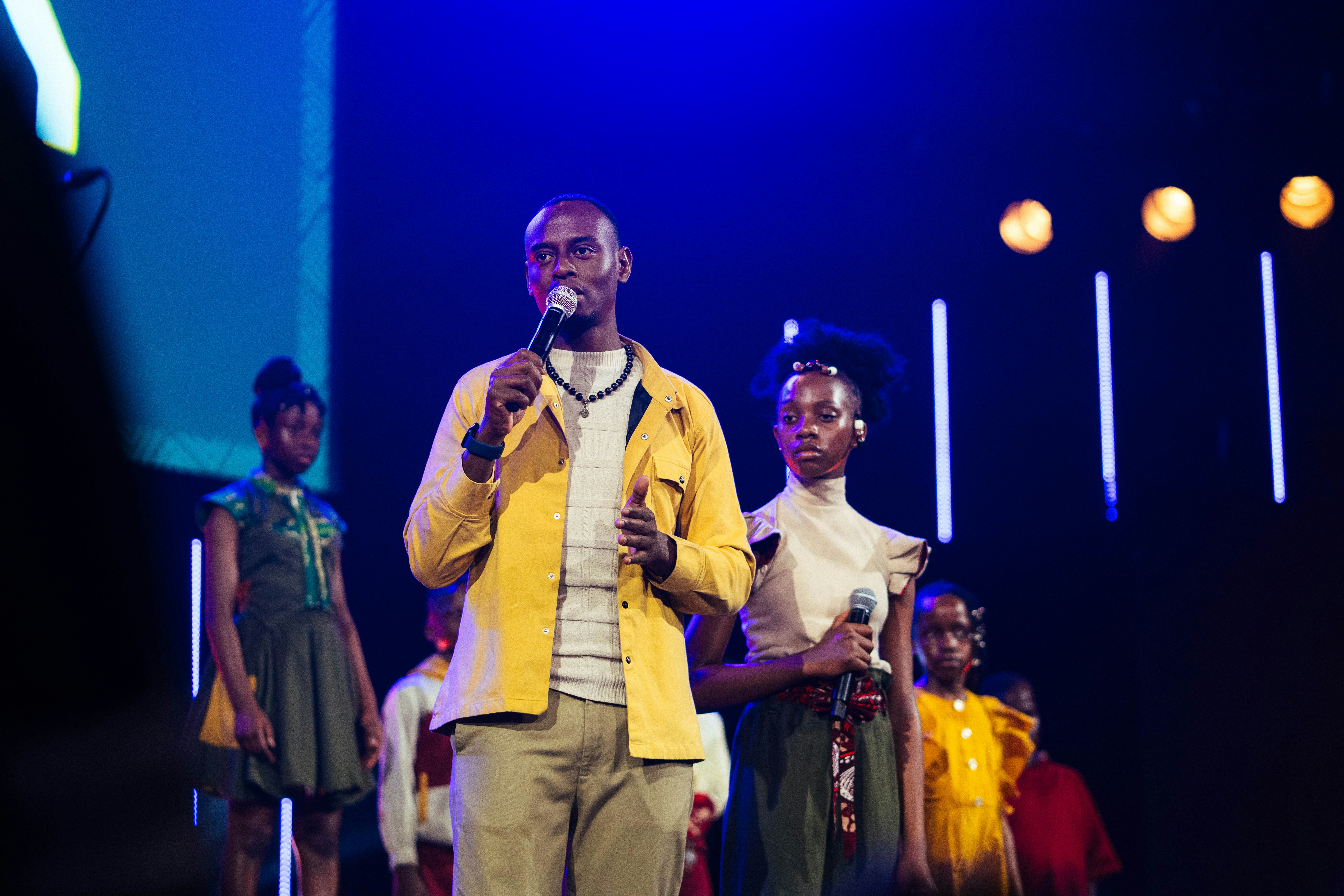 A man is speaking with children on a stage.