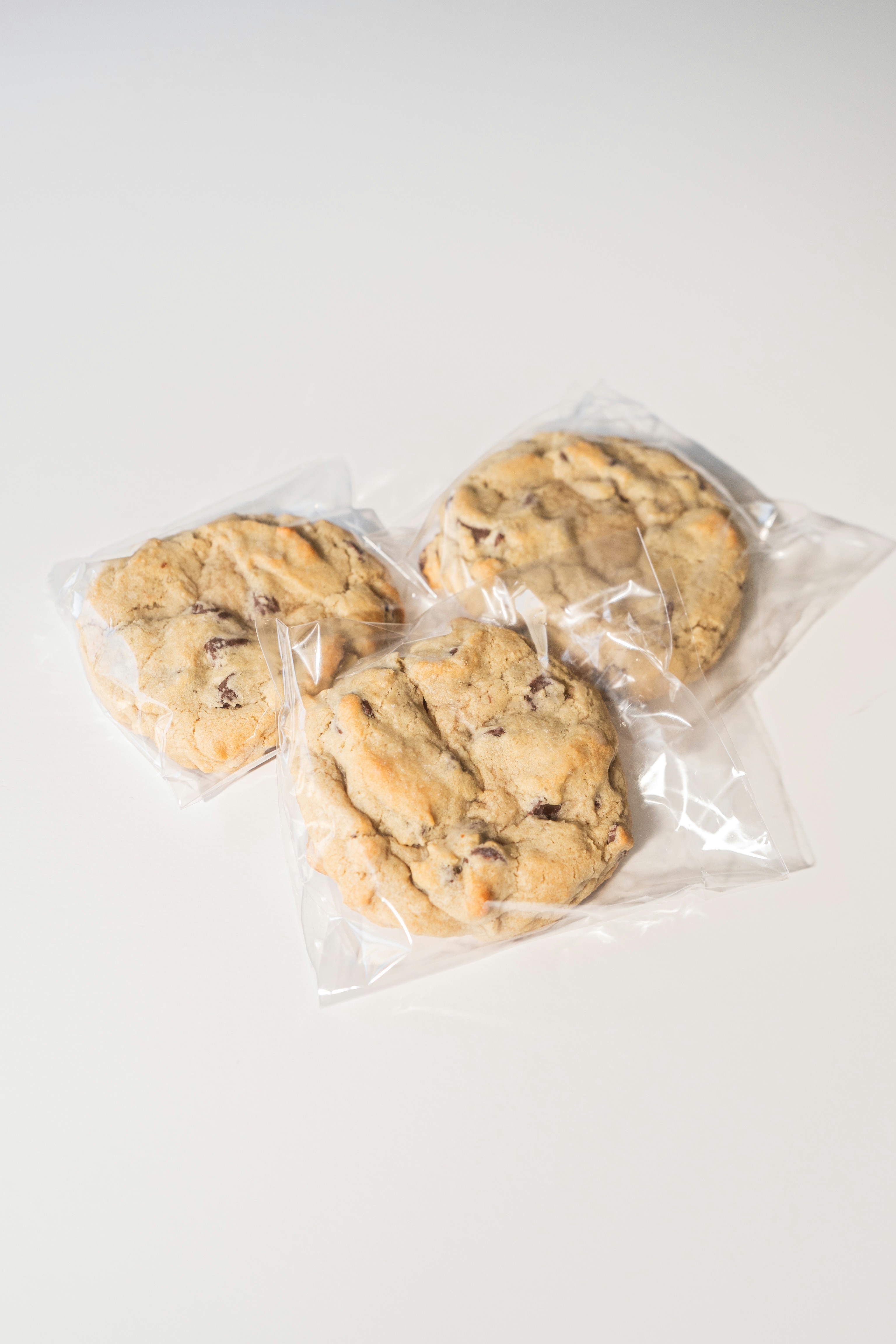 Three chocolate chip cookies are wrapped in plastic.