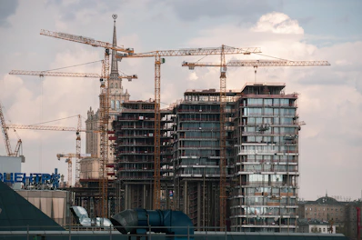 Construction cranes build skyscrapers against a cloudy sky.