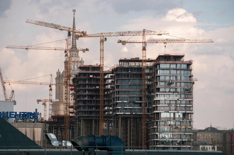 Construction cranes build skyscrapers against a cloudy sky.