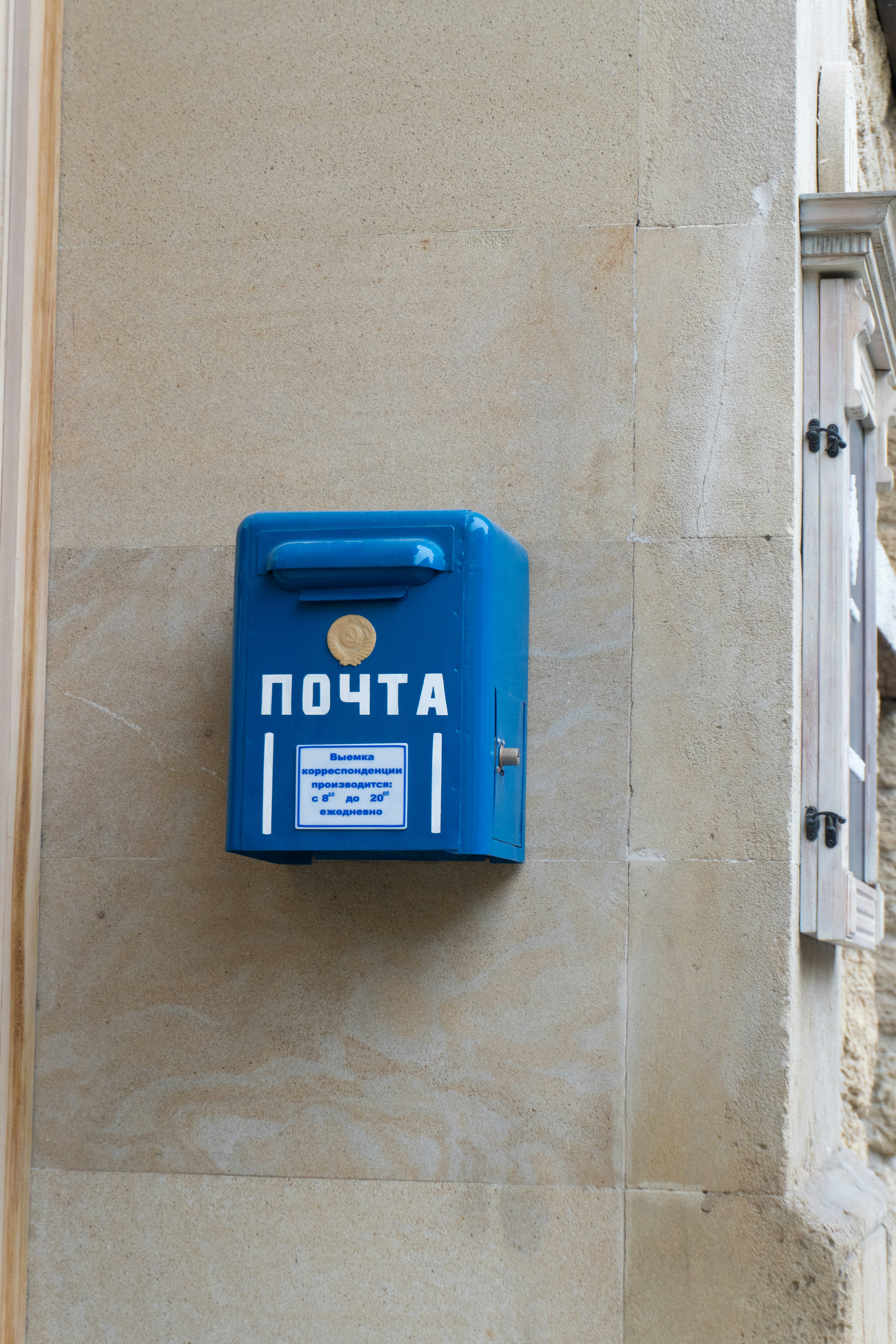 Blue mailbox with russian writing is attached to a wall.