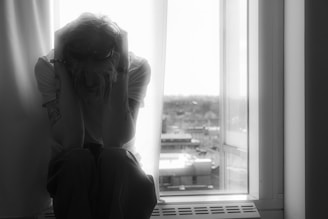 A person is depressed, sitting by the window.