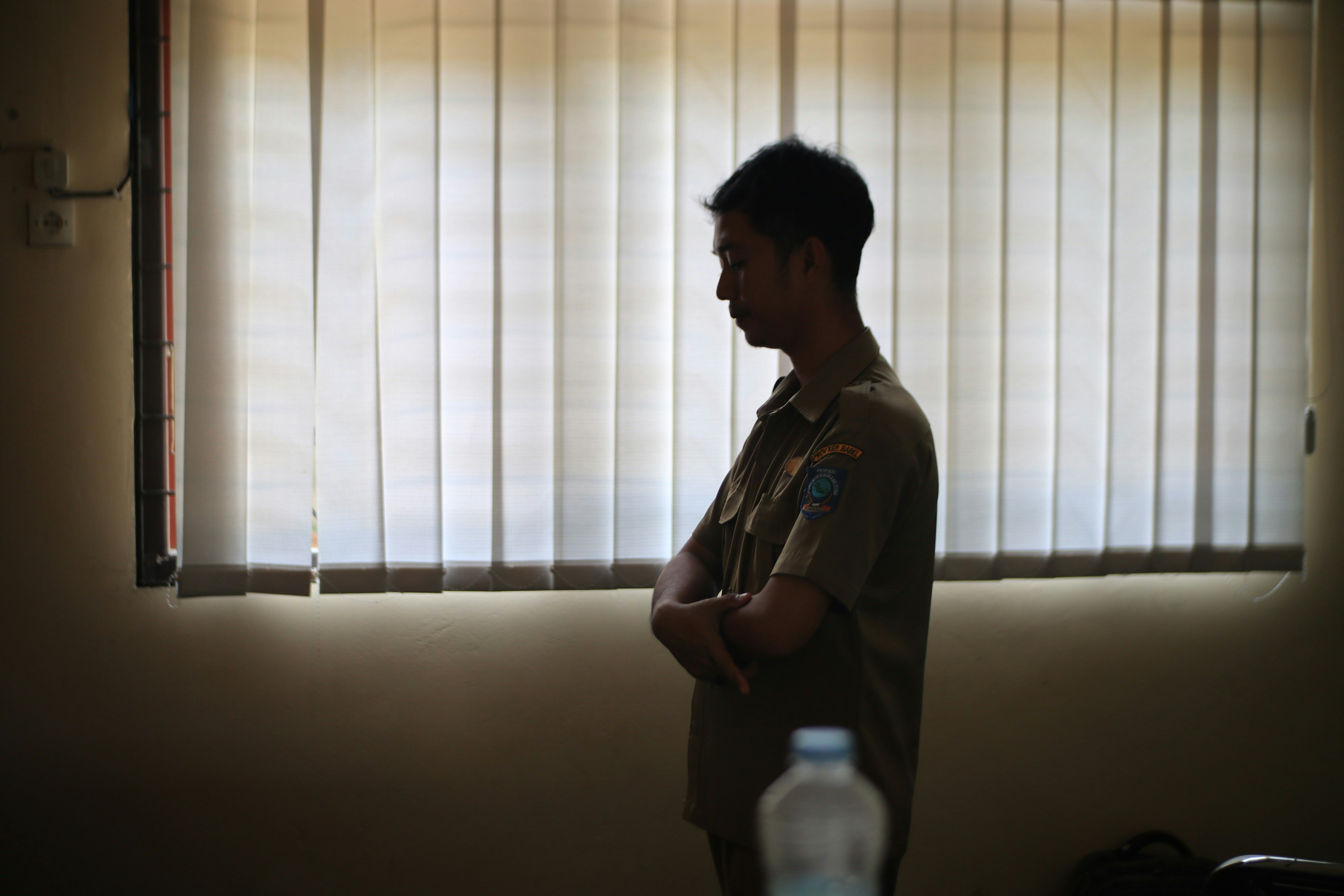 Man stands in front of a window with blinds.
