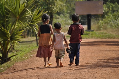 Three children walk along a dirt path.