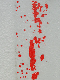 Red paint splatters and streaks on a white wall.