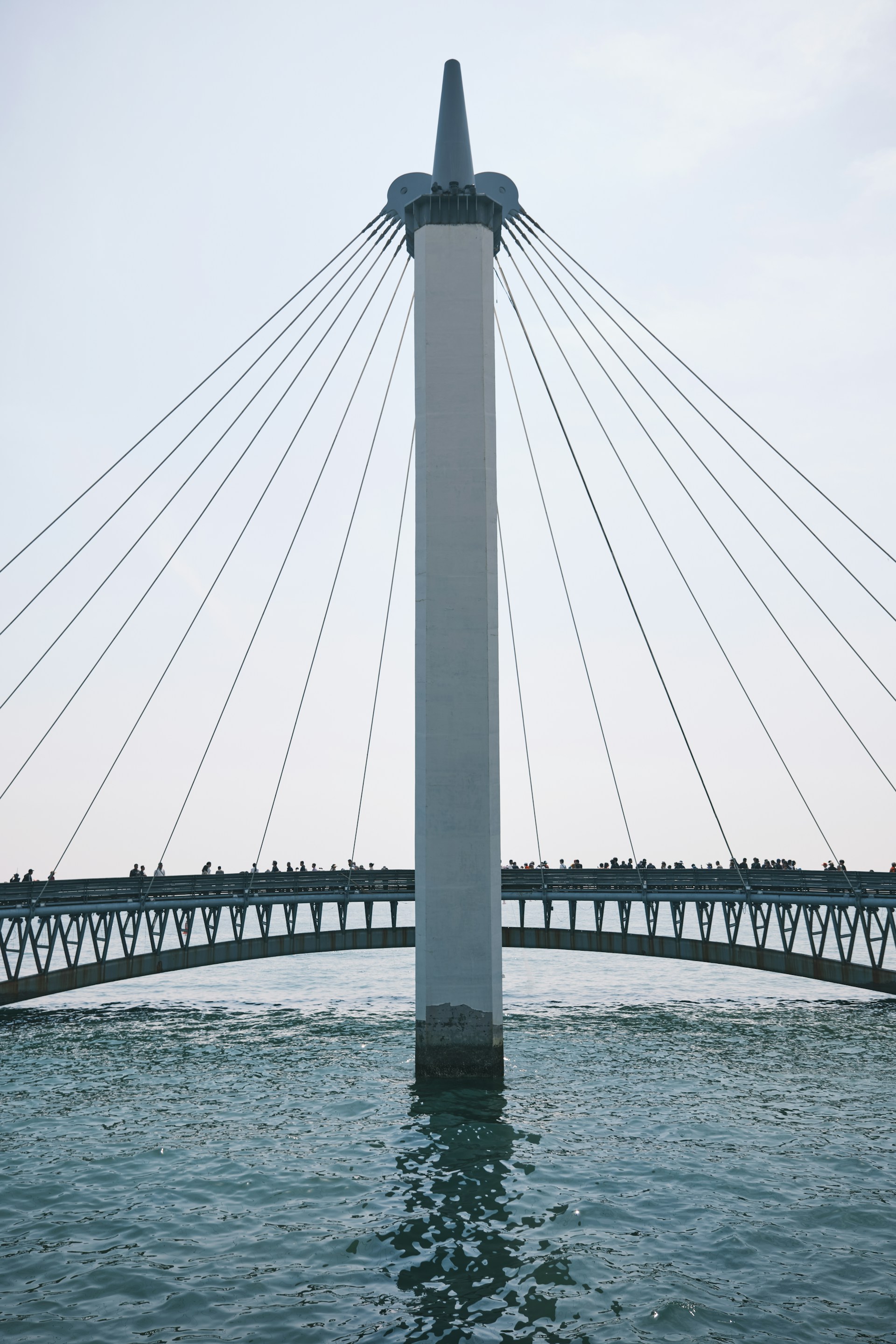 A tall, white tower supports a bridge over water.