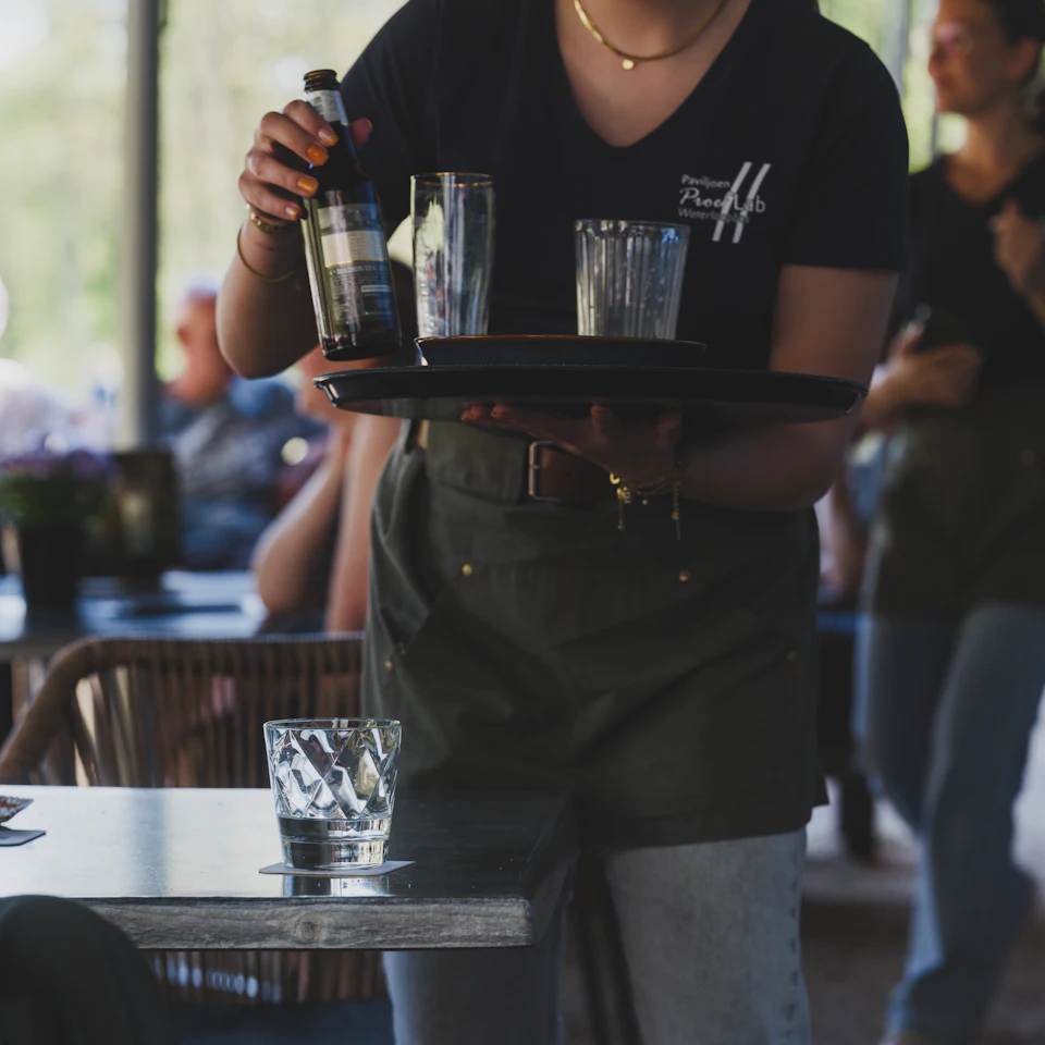 Una camarera lleva una bandeja con vasos entre las mesas de un restaurante.