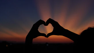Hands form a heart shape against the sunset