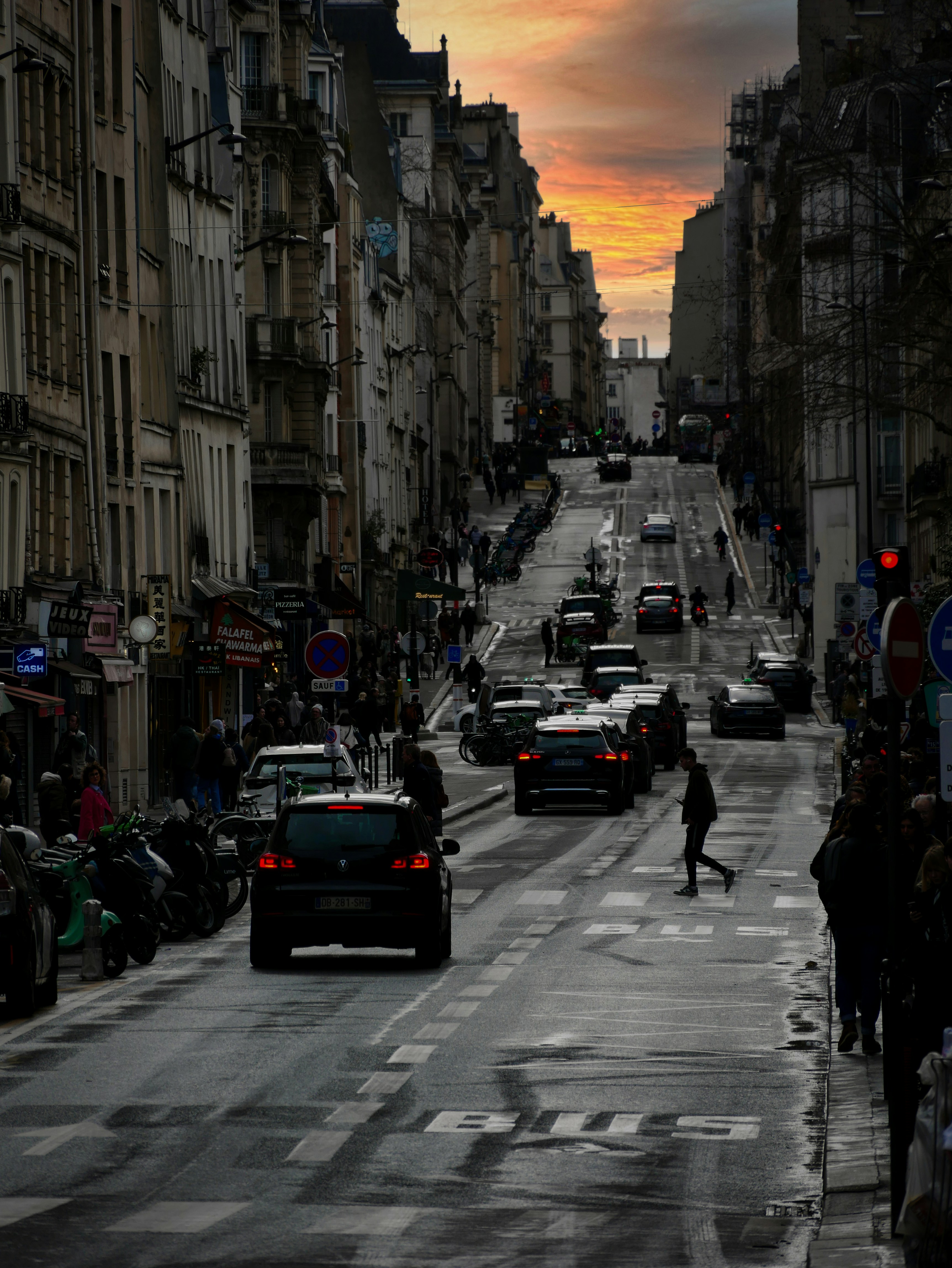 A city street leads to a sunset sky.