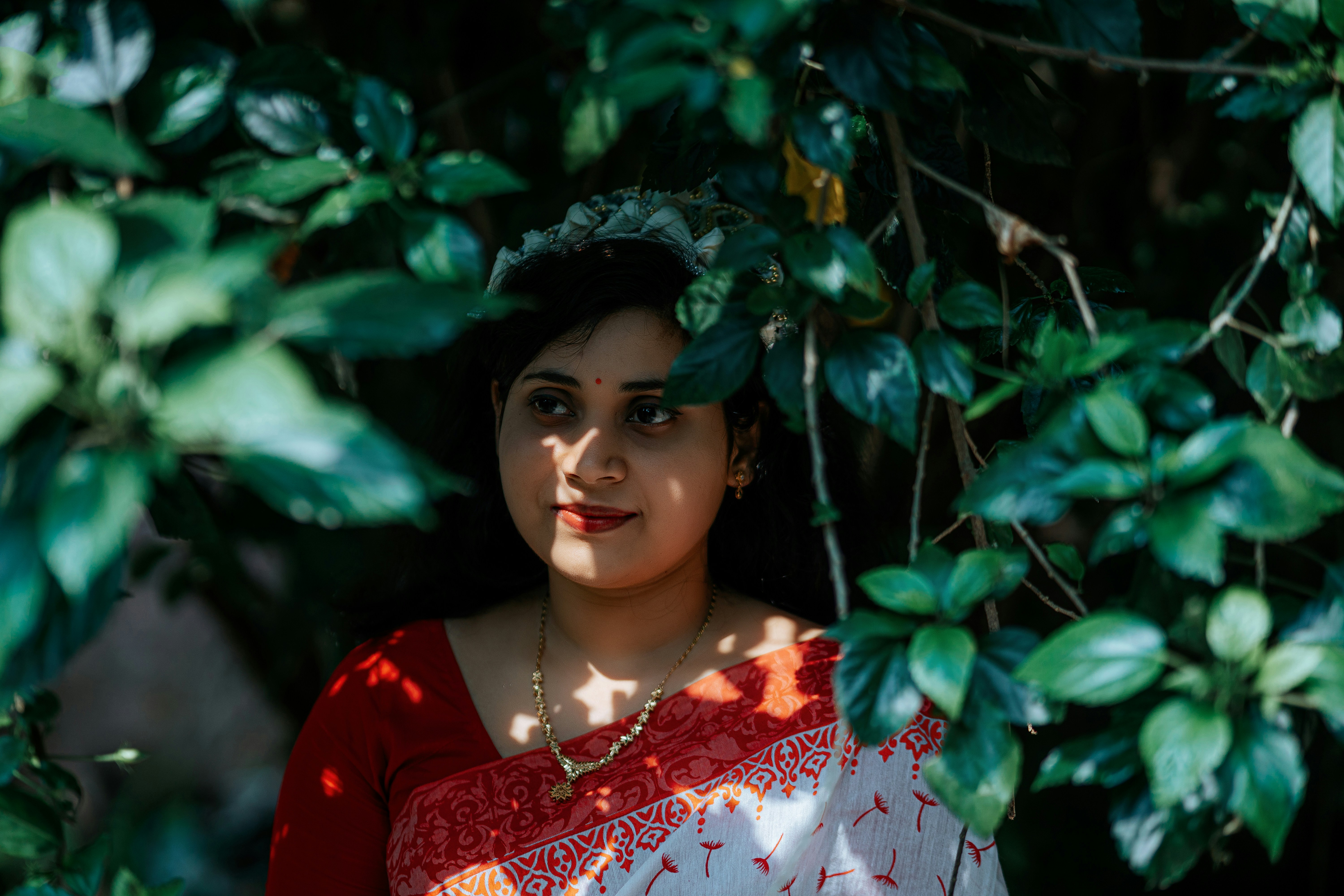 Woman poses behind leafy green foliage.