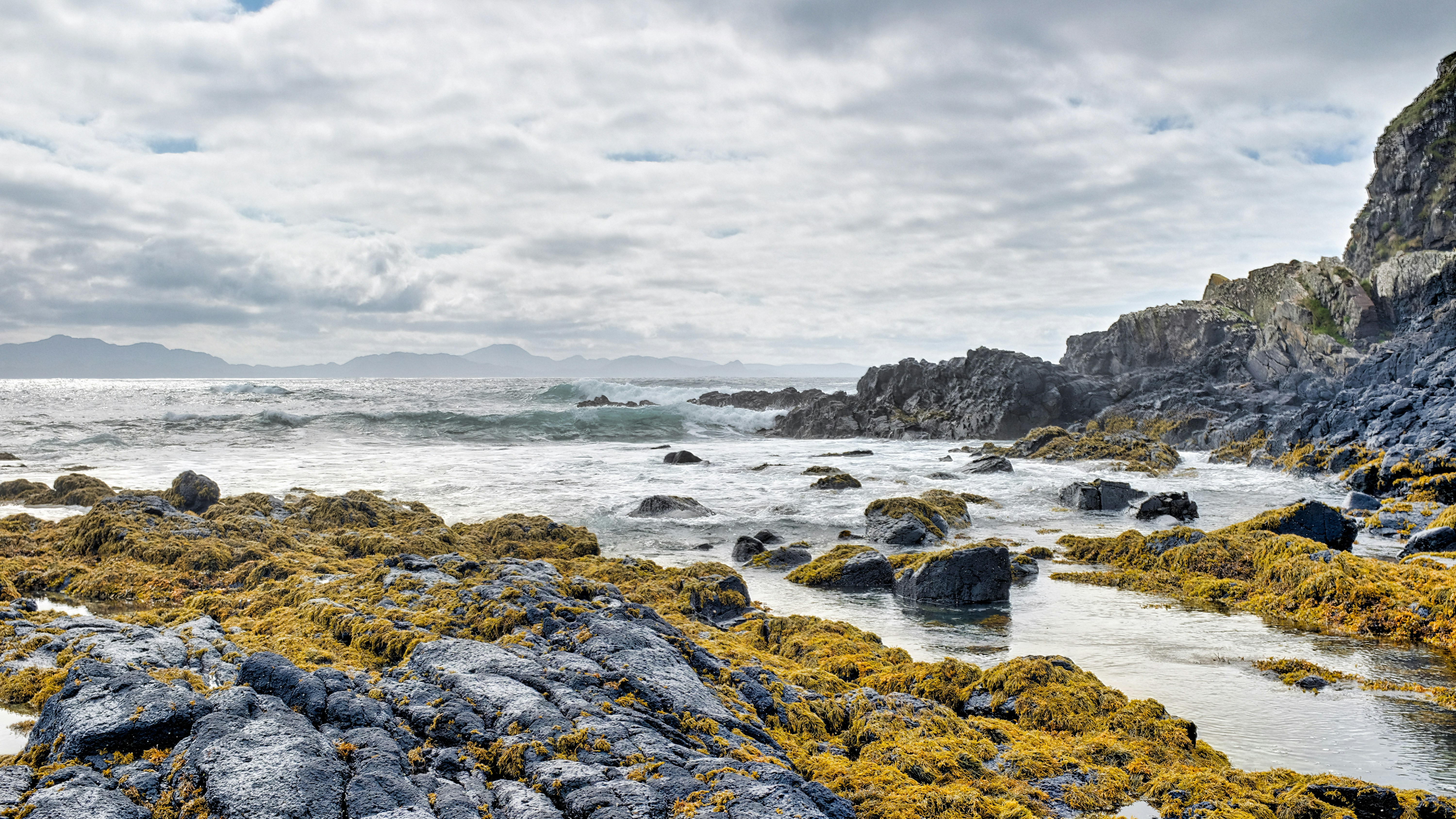 Rocky coastline with ocean waves under cloudy sky.