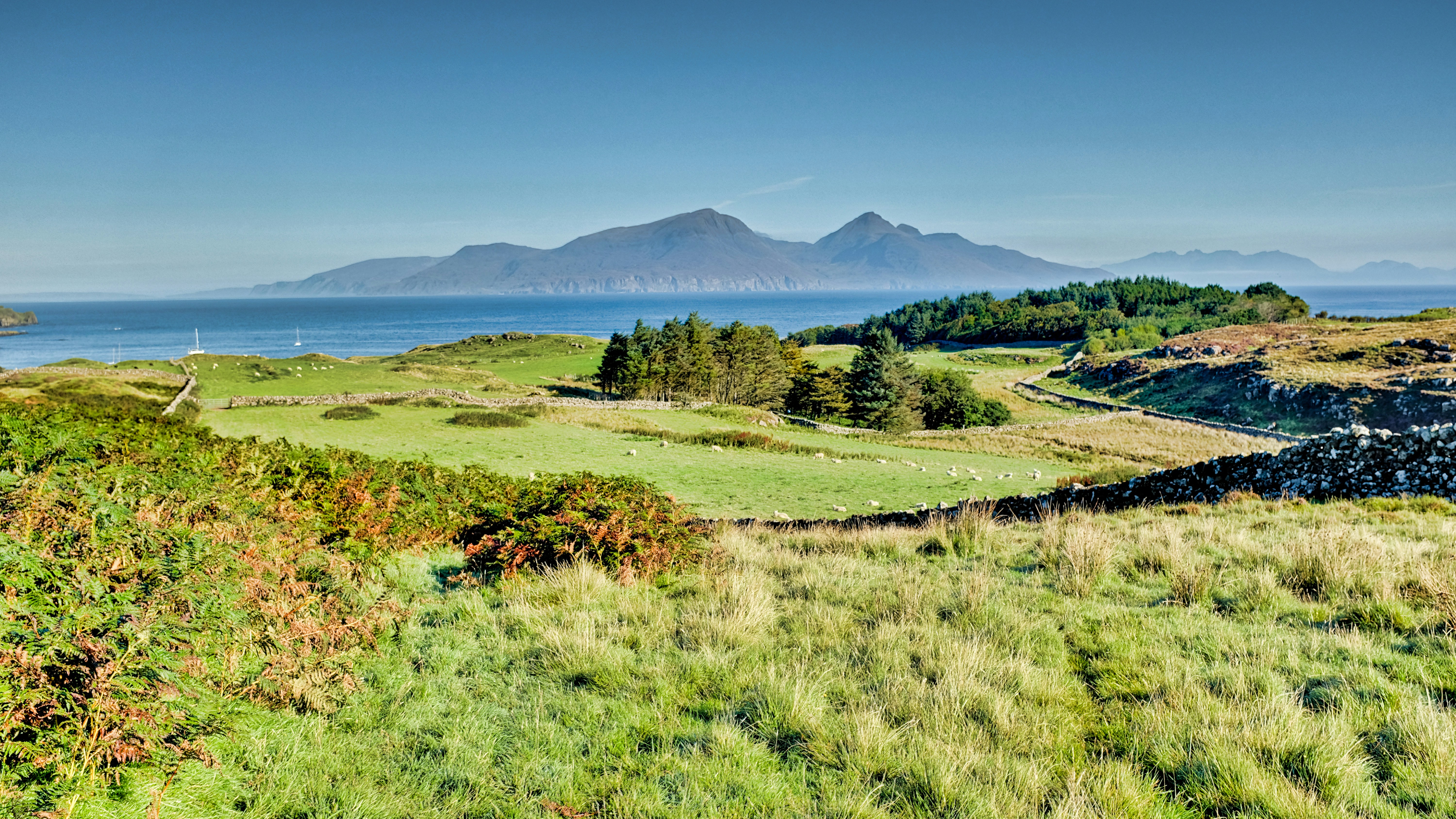 Scenic view of mountains, sea, and green meadows.