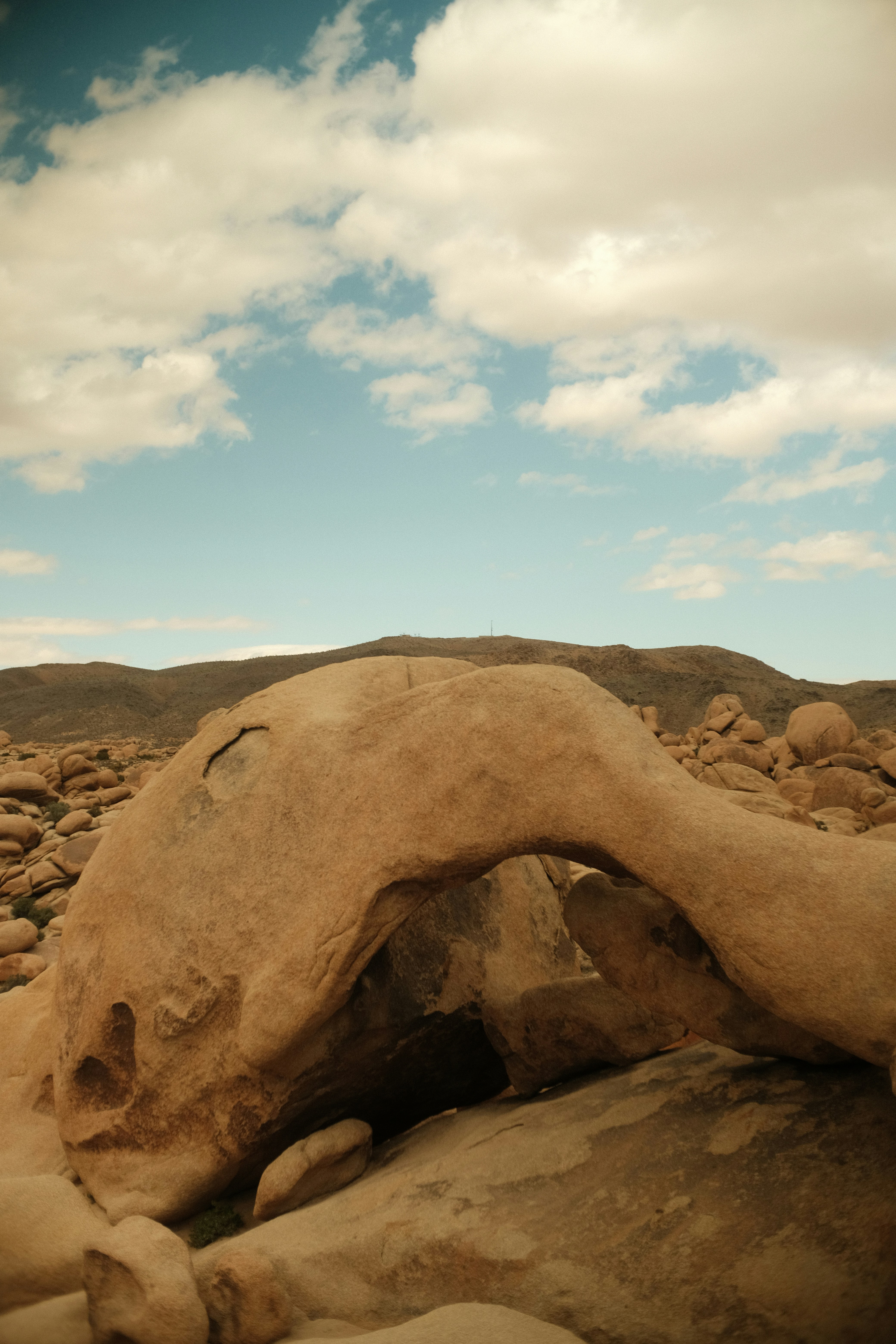 A rock formation arches under a cloudy sky.