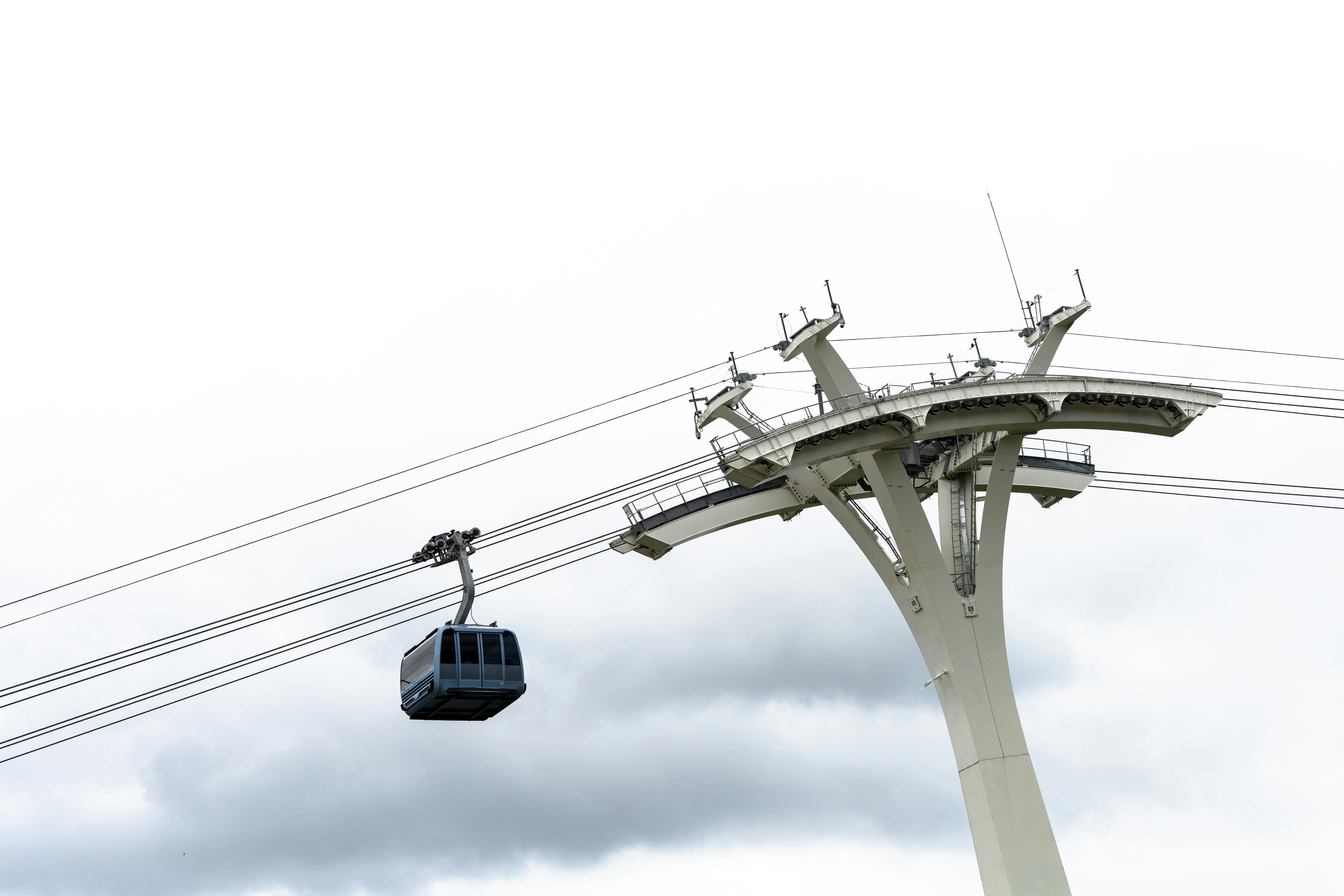 Cable car travels near a modern, white tower.