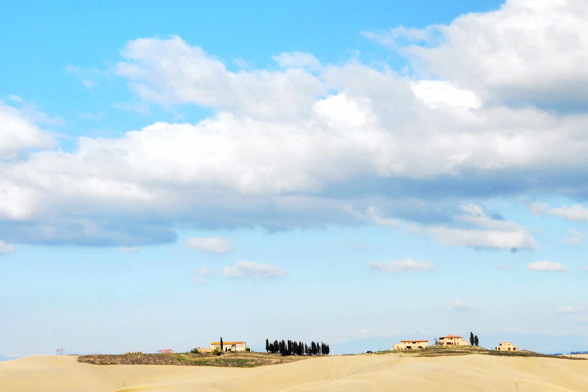 Clouds over the bare rolling hills of the Crete Senesi, with farmhouses and cypresses on the ridge