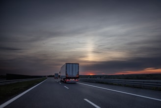 Trucks drive on a highway at sunset.