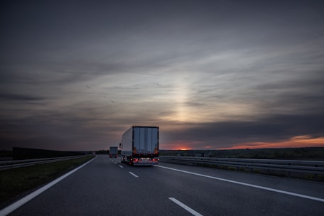 Trucks drive on a highway at sunset.