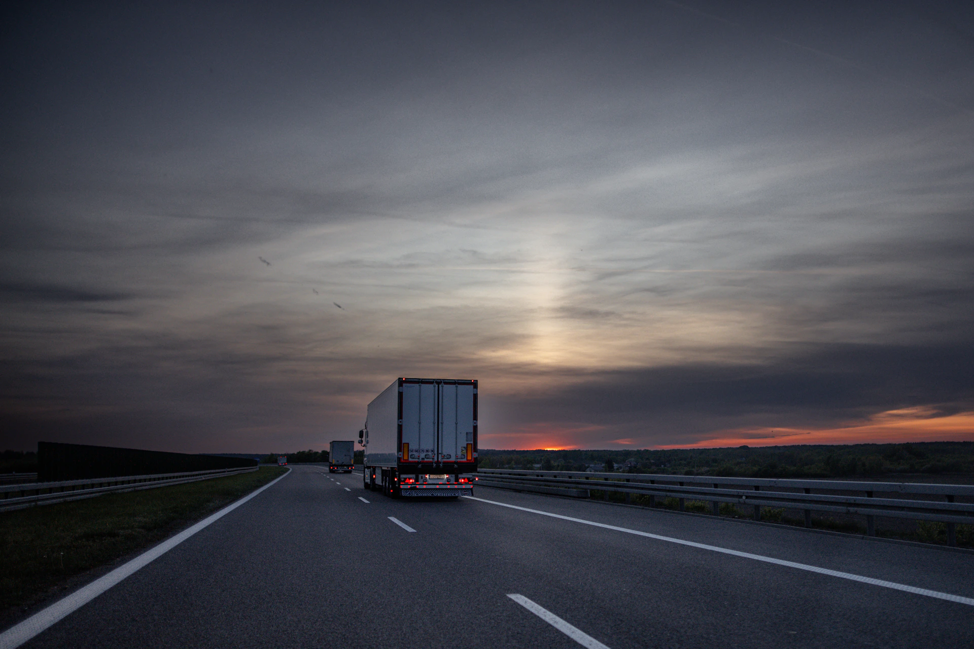 Trucks drive on a highway at sunset.