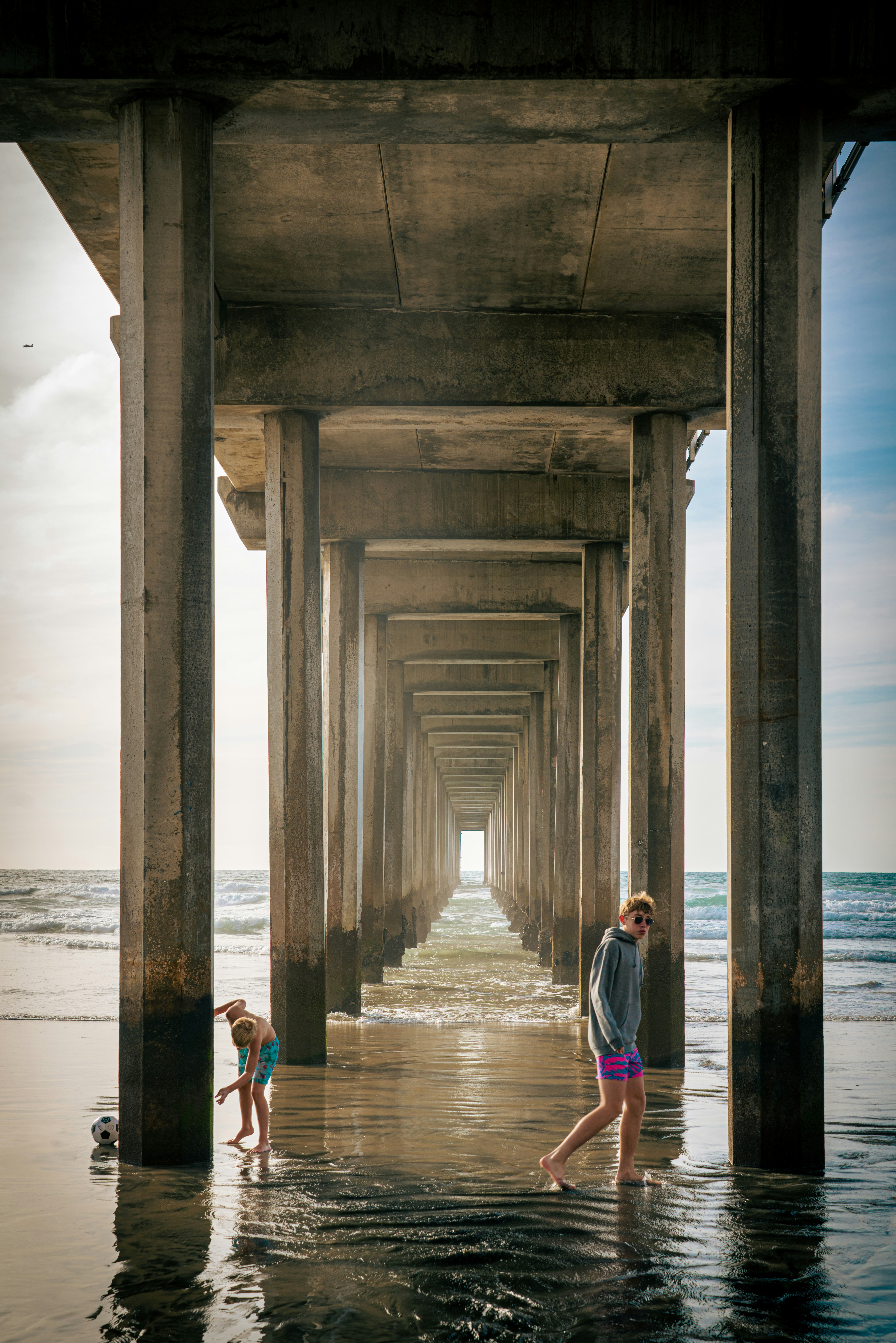 People walk and play under a pier at the beach.