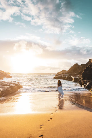 Woman walks along a beach toward the ocean.