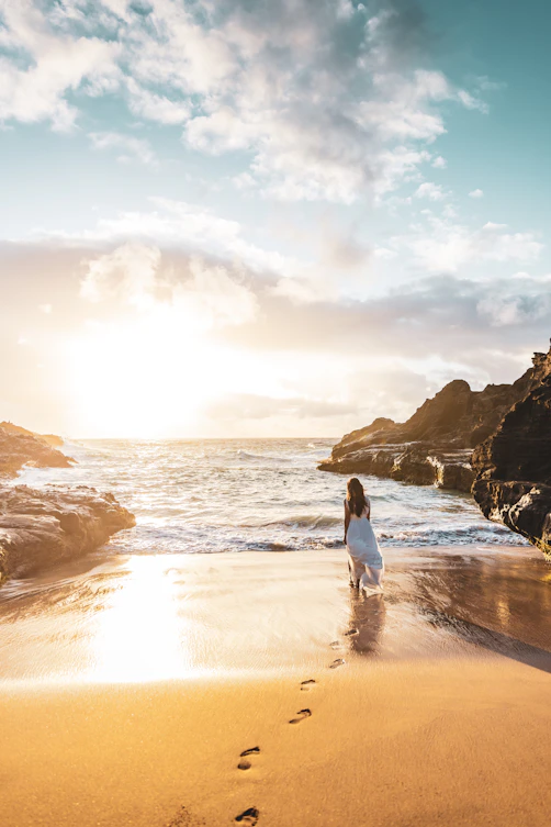 Woman walks along a beach toward the ocean.