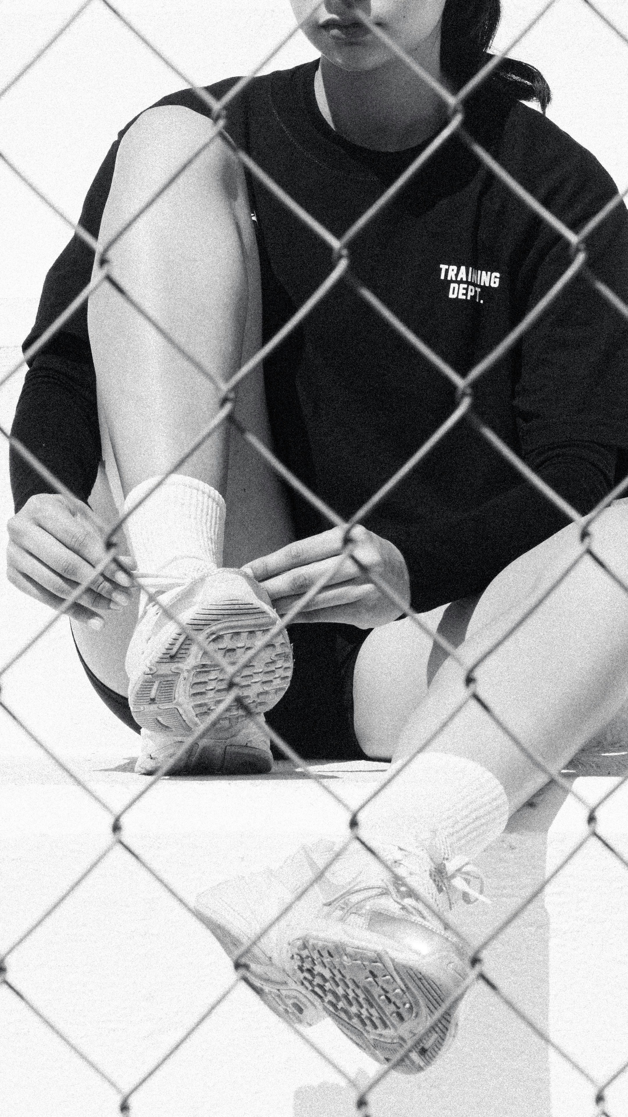 Person tying shoelaces through a chain-link fence.
