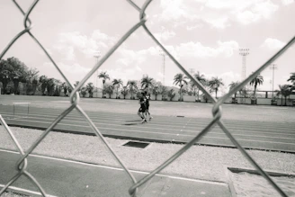 Two people running on a track behind a fence