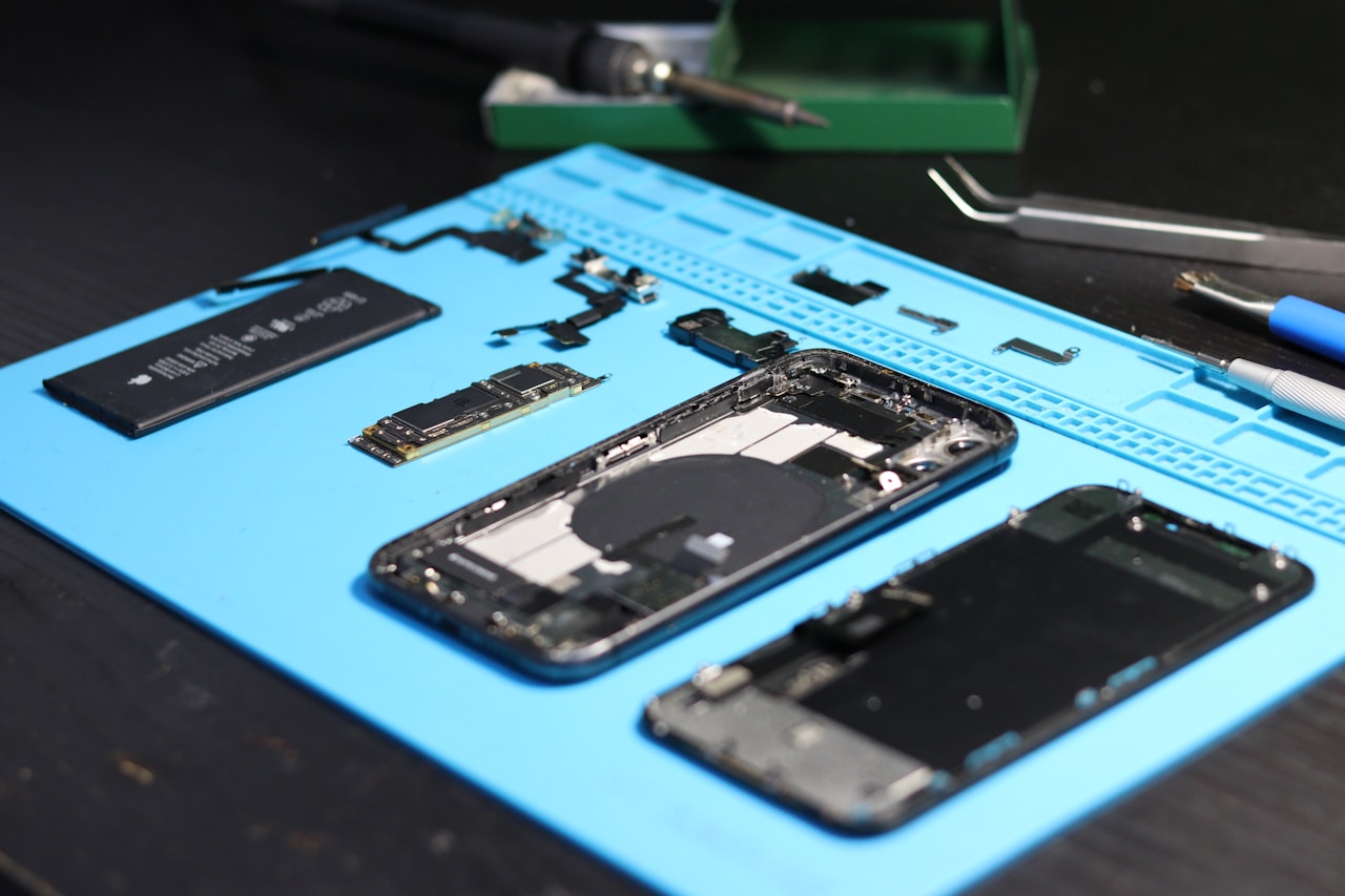 Open smartphone internals laid out on a white lab bench — PCB, NAND flash, CPU/SoC, camera module and battery side by side — reference to the engineer's review of which layer of a domestic-manufacturing claim can actually be domestic