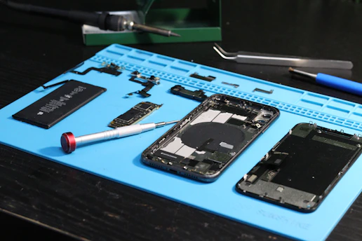 Componentes e ferramentas para reparo de telefones estão dispostos ao redor.