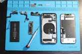 iPhone components are disassembled on a blue mat.