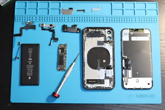 iPhone components are disassembled on a blue mat.