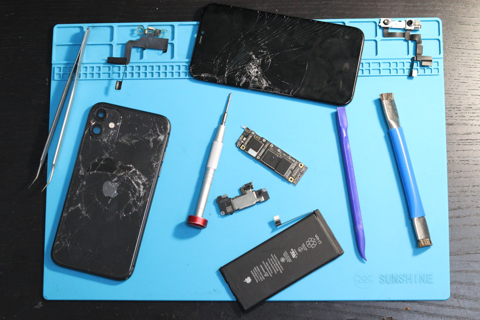 A disassembled smartphone with repair tools laid out on a mat