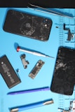 Broken iphones with repair tools on a blue mat.