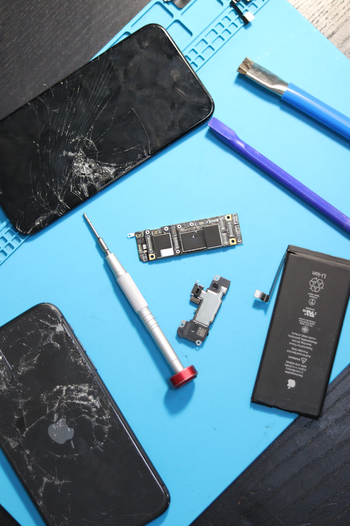 Bancada de assistência técnica com celular aberto, placa, bateria e chave de precisão