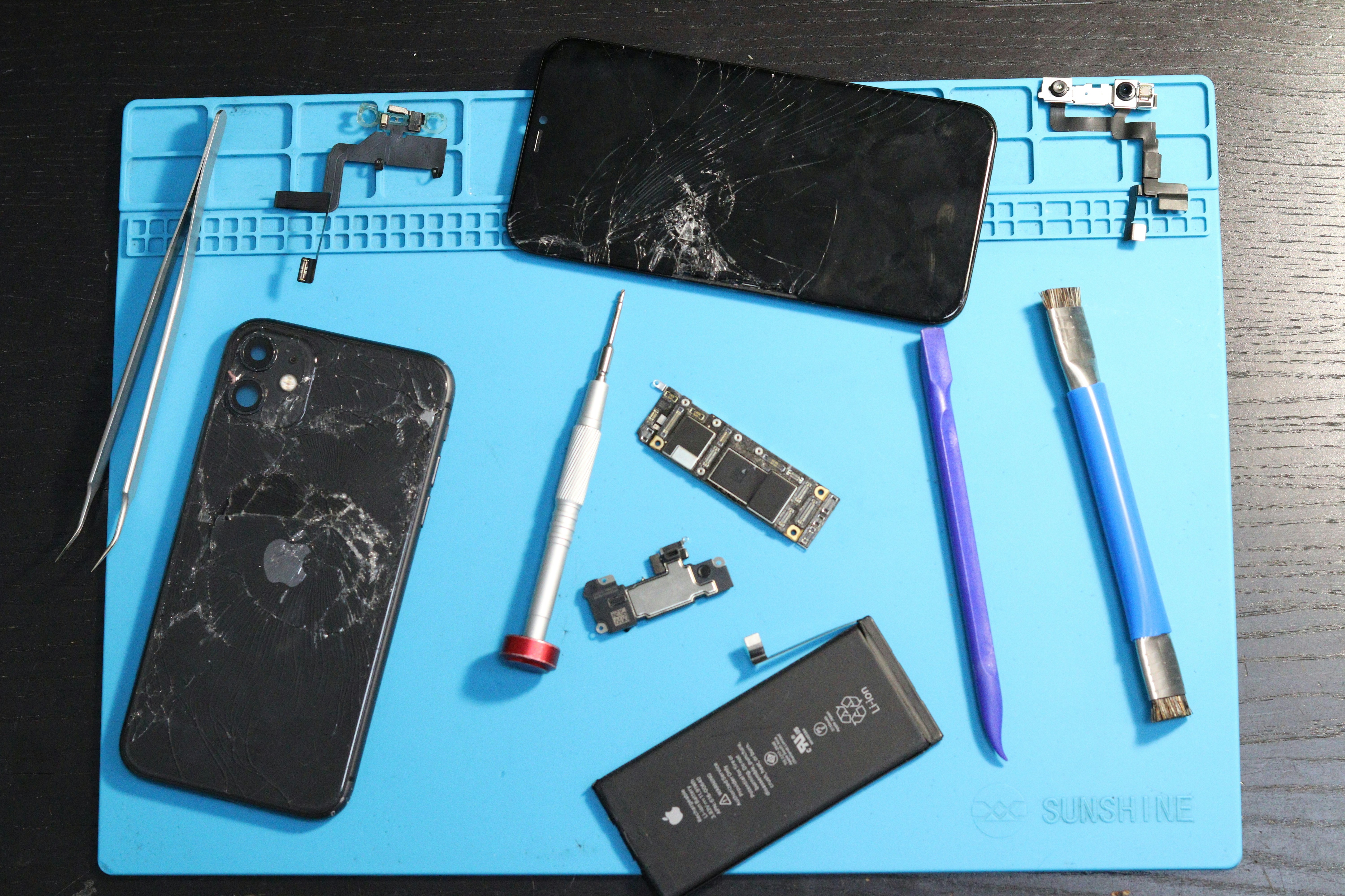 Cracked iphones and repair tools arranged on a mat.