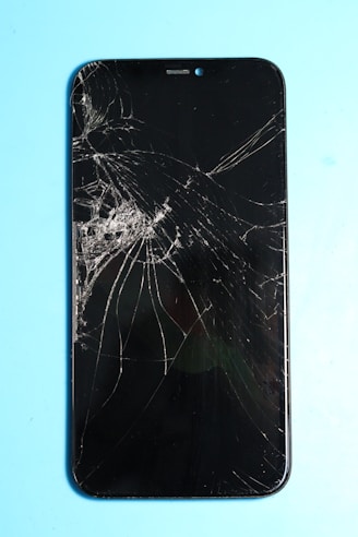 Broken smartphone screen on a blue surface.