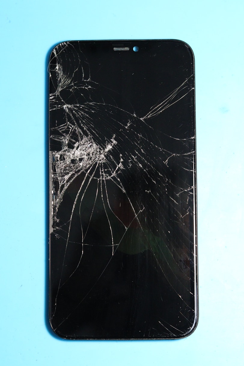 Broken smartphone screen on a blue surface.