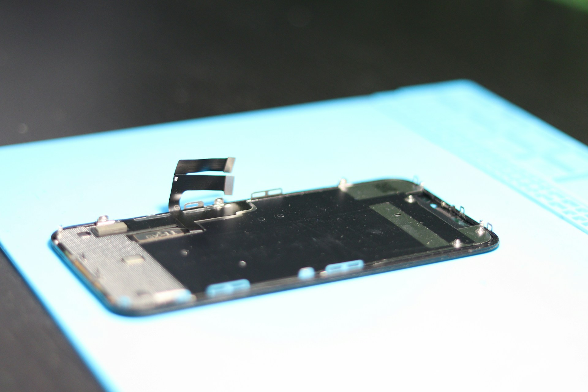 Disassembled phone screen on a blue mat.